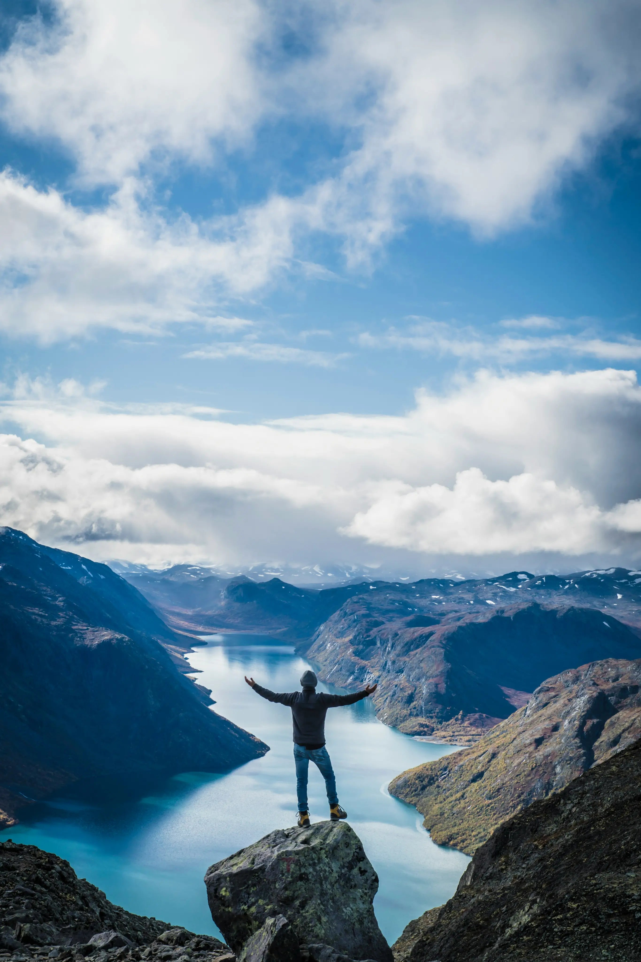 Person standing on a cliff overlooking a scenic landscape with mountains and a lake.