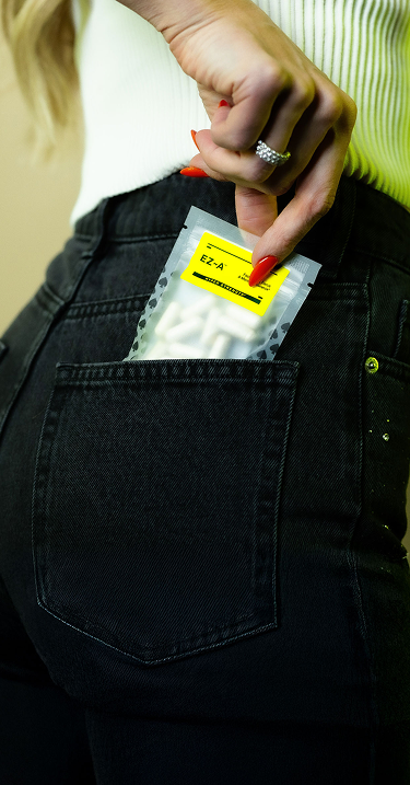 Hand holding a small package with a yellow label over a black pocket.