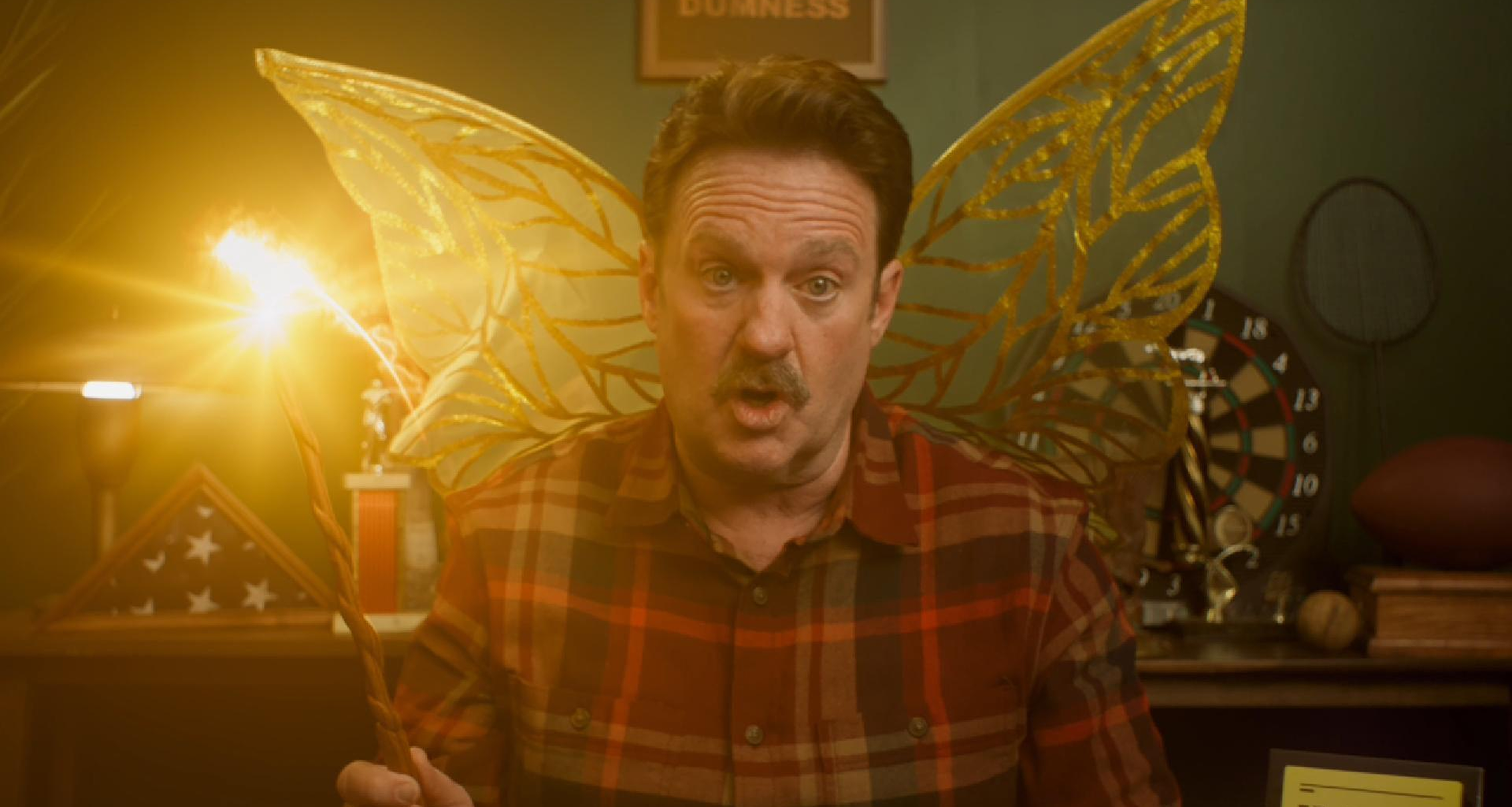 Man with butterfly wings holding a mug in a dimly lit room
